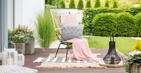 Comfortable outdoor chair with blankets and pillows on it in a well manicured back yard