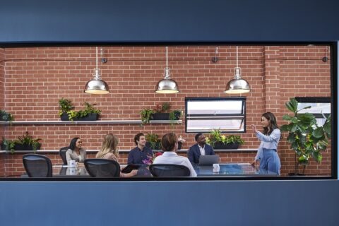 Woman presenting in brick walled conference room to table of people listening
