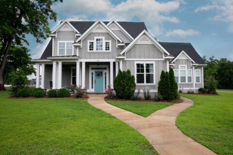 exterior of luxury home, grey in color with light blue front door and manicured front lawn